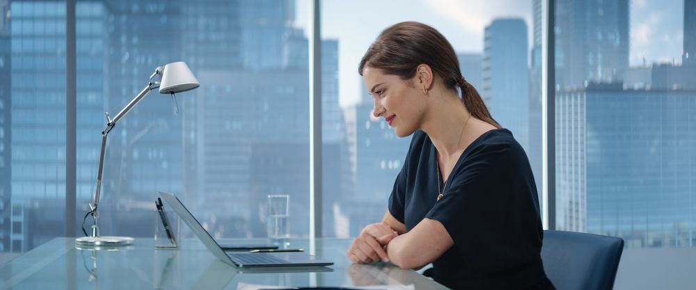 Portrait of Successful Young White Businesswoman Sitting at Her Desk Working on Laptop in Big City Office.