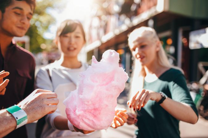 Three young people sharing cotton candy at amusement park