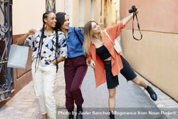 Three happy women walking down narrow lane and taking photos with camera 48r8q0