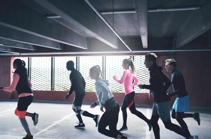 Side view of men and women running together in industrial space