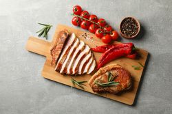 Board with fried steaks on gray background. Grilled food