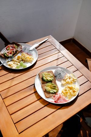 Casual breakfast table set in the sun with eggs, fresh fruit, and avocado toast