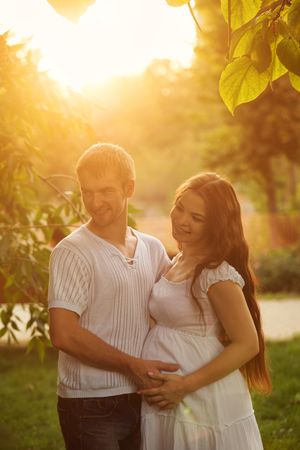 Happy pregnant woman with her partner pictured under trees at magic hour