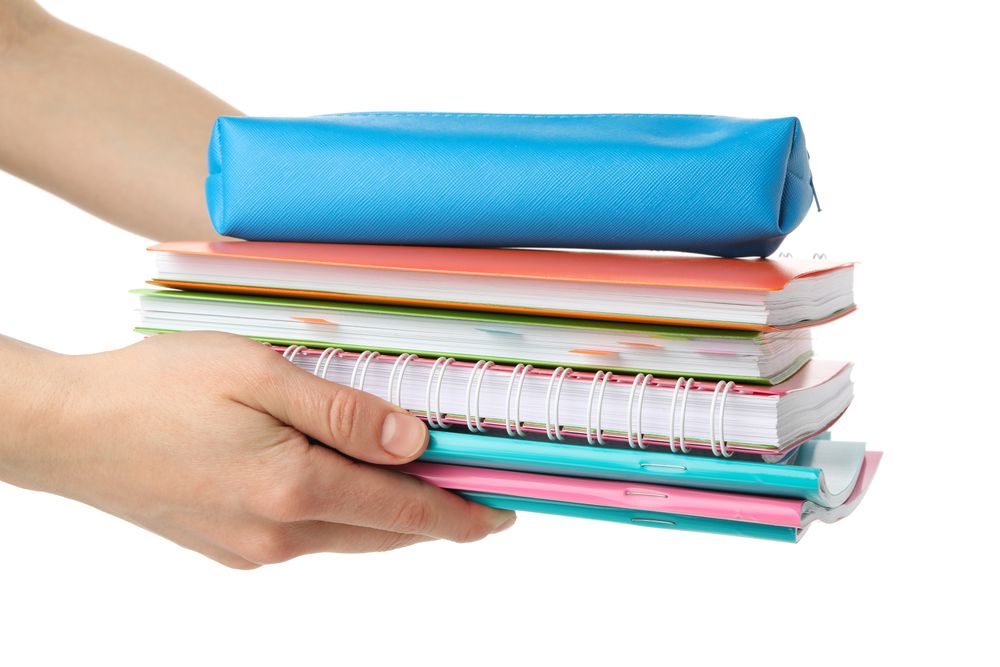 Hands holding pile of books and notebooks
