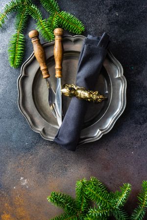 Dark plate with knife and fork with pine branch and napkin with golden ring