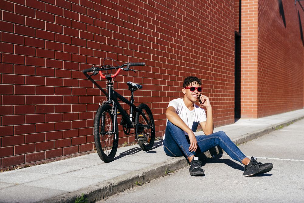 Young happy Black male talking smartphone near bike