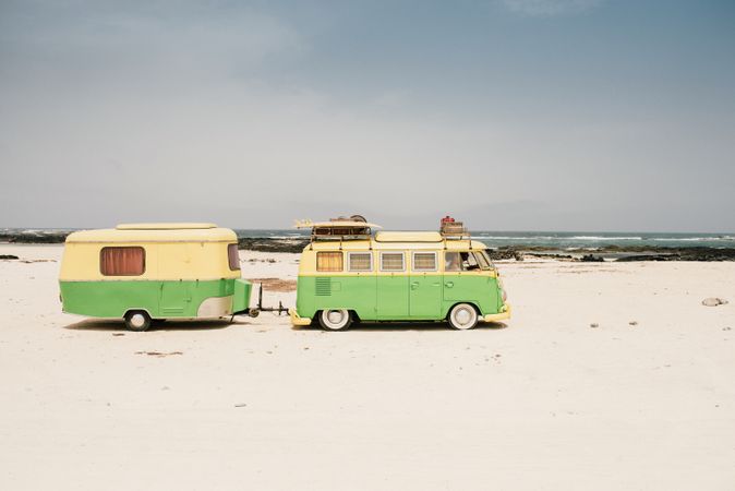 Colorful minibus with trailer parked on sandy shore in sunny day