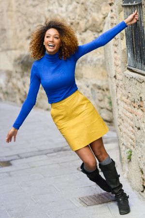Happy female with curly hair wearing bright blue shirt holding bars on window on street