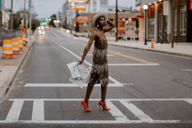 Black woman in red heels holding a newspaper walking across the crosswalk