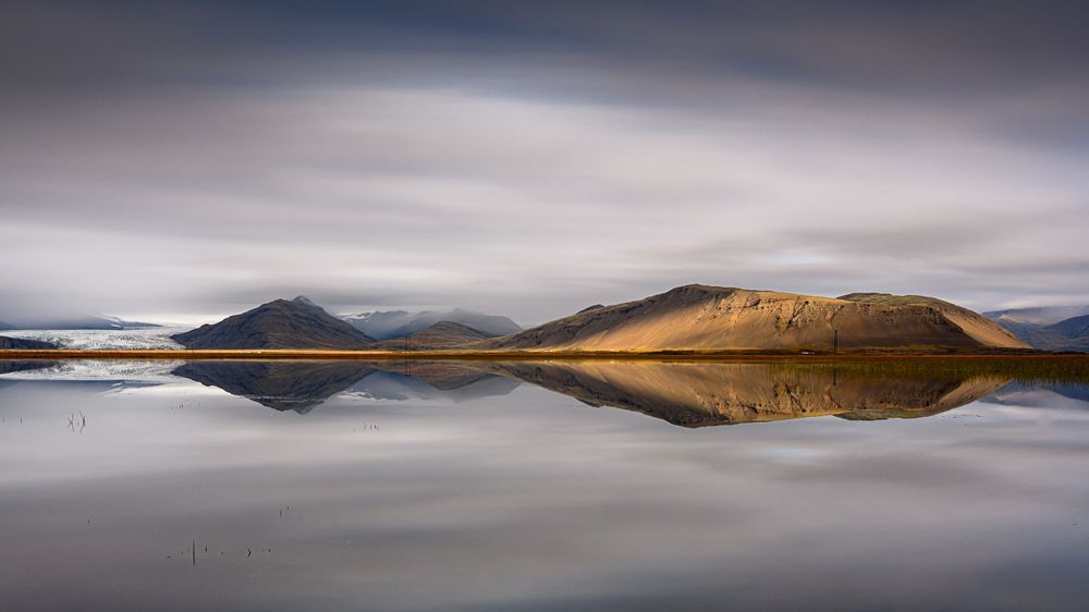 Brown mountain near body of water under cloudy sky
