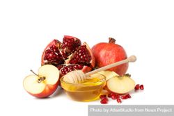 Side view of pot of honey with dipper, split pomegranate and apples 5zMDk0