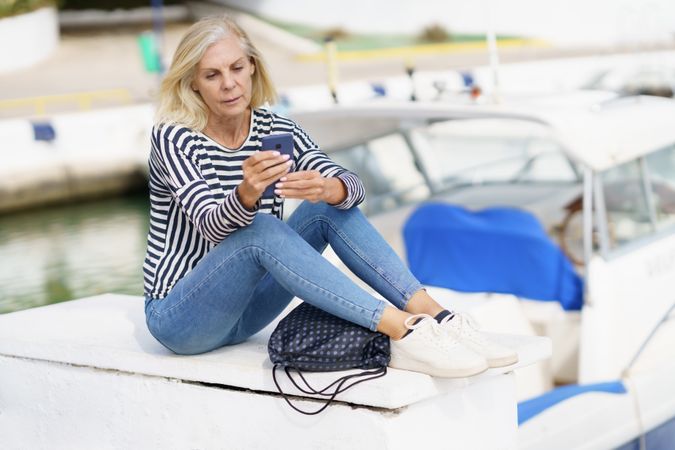 Mature woman using her smartphone sitting on the dock