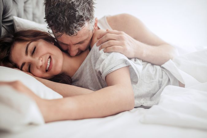 Man kissing on neck of woman, both lying on bed