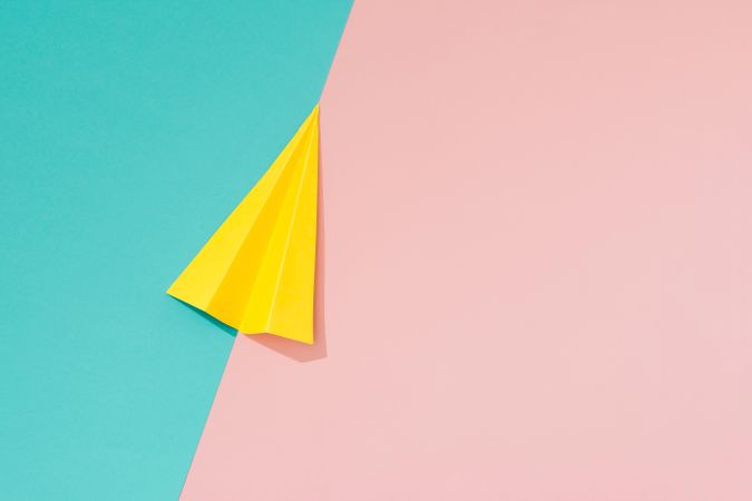 Yellow paper airplane on pastel pink and blue background