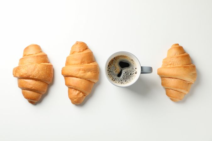 Flat lay with croissants and cup of coffee on plain background, top view