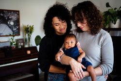 Two new mothers holding and looking down on their newborn baby girl