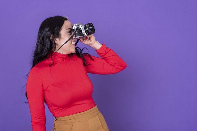 woman taking a photo with her film camera over a violet background.