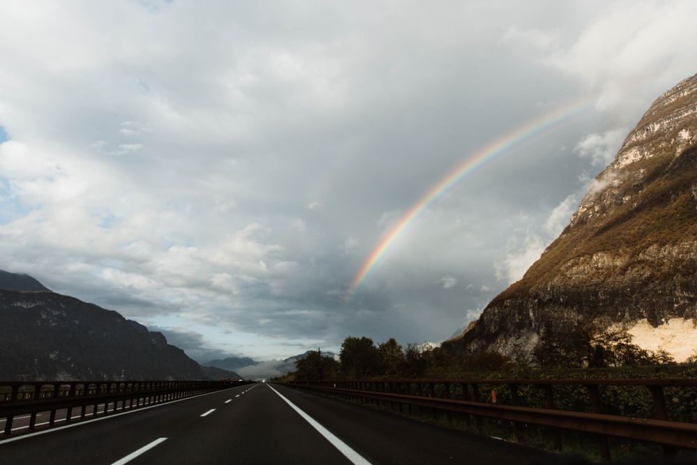 Lonely highway amid mountains and sky with rainbow