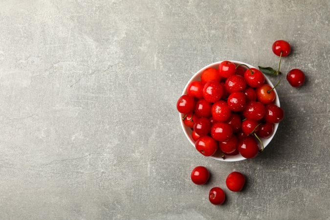 Bowl with red cherry on gray background, top view