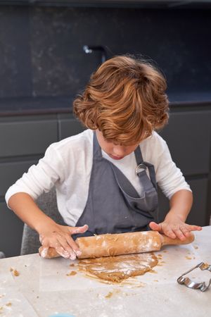 Serious child kneading dough with rolling pin at home