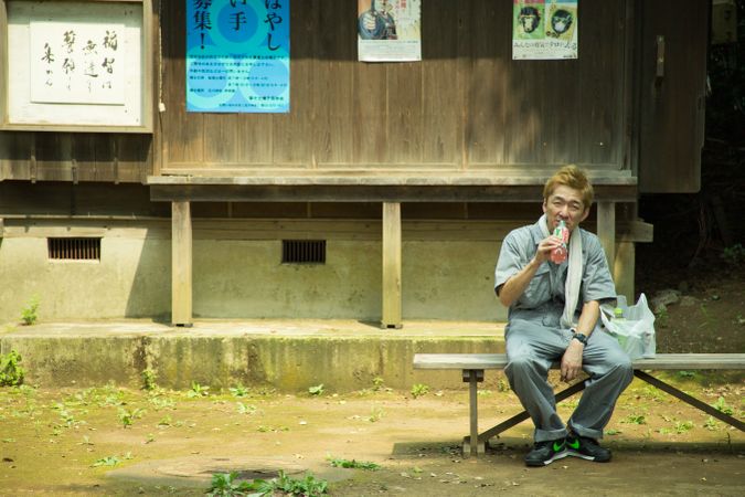 Worker taking a lunch break sitting beside plastic bag on wooden bench outdoor