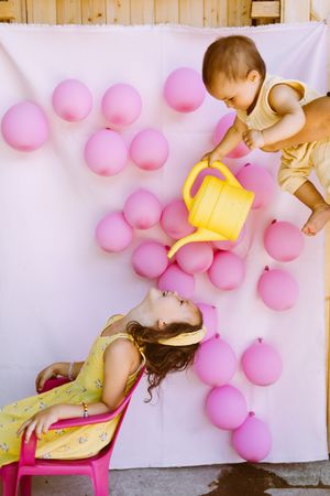 Kids having fun with watering can against wall with balloons