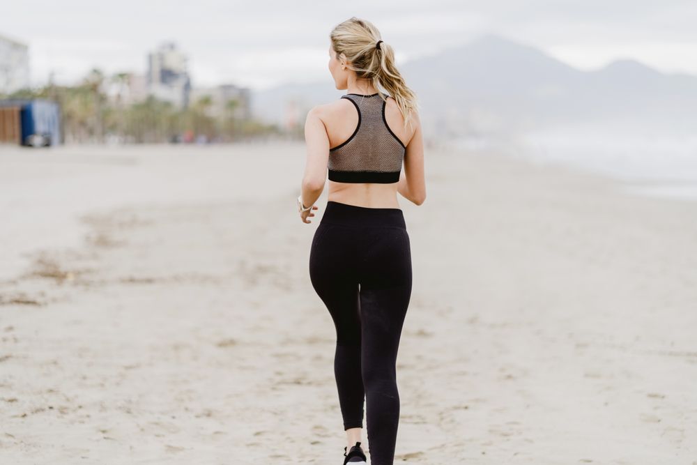 Female runner in stylish sportswear jogging along calm sandy seaside