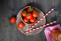Top view of bowl of fresh tomatoes with straws and juice