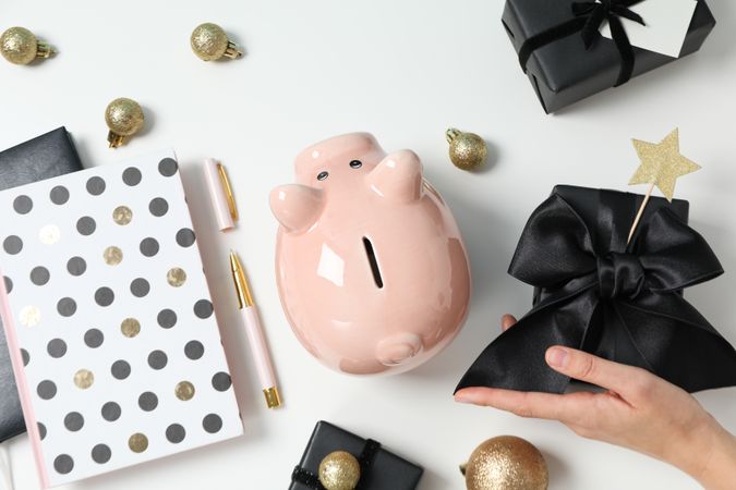 Piggy bank, balls, gift boxes and female hand on neutral background, top view