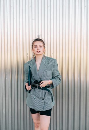 Woman with tablet in stylish suit standing nearby wall holding sunglasses
