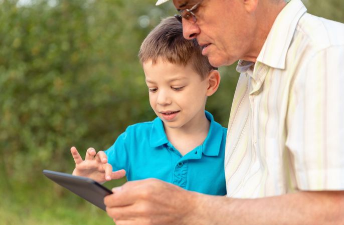 Grandchild and grandfather using a tablet in park outdoors