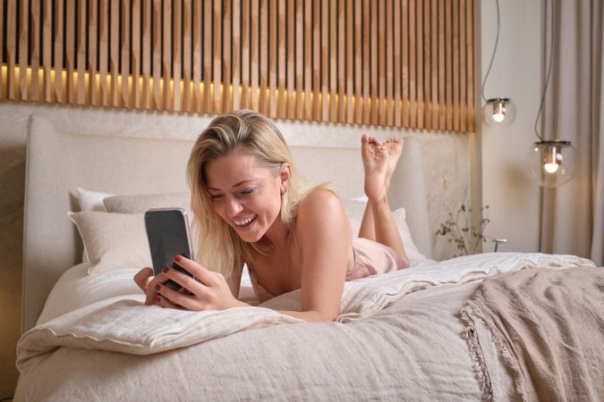 Young female laughing while browsing smartphone in bed