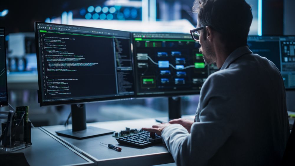 Back View of a Young Engineer Working on Computer in a Technological Office Environment. Male Programmer Writing Software Code for a Blockchain Project, Developing Backend System