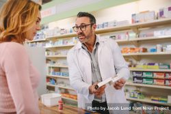 Male pharmacist holding medicine box giving advice to female customer in chemist shop 0g7EX0