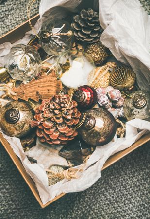 Wooden box of rustic holiday tree decorations, pine cones, balls and baubles laying on tissue paper