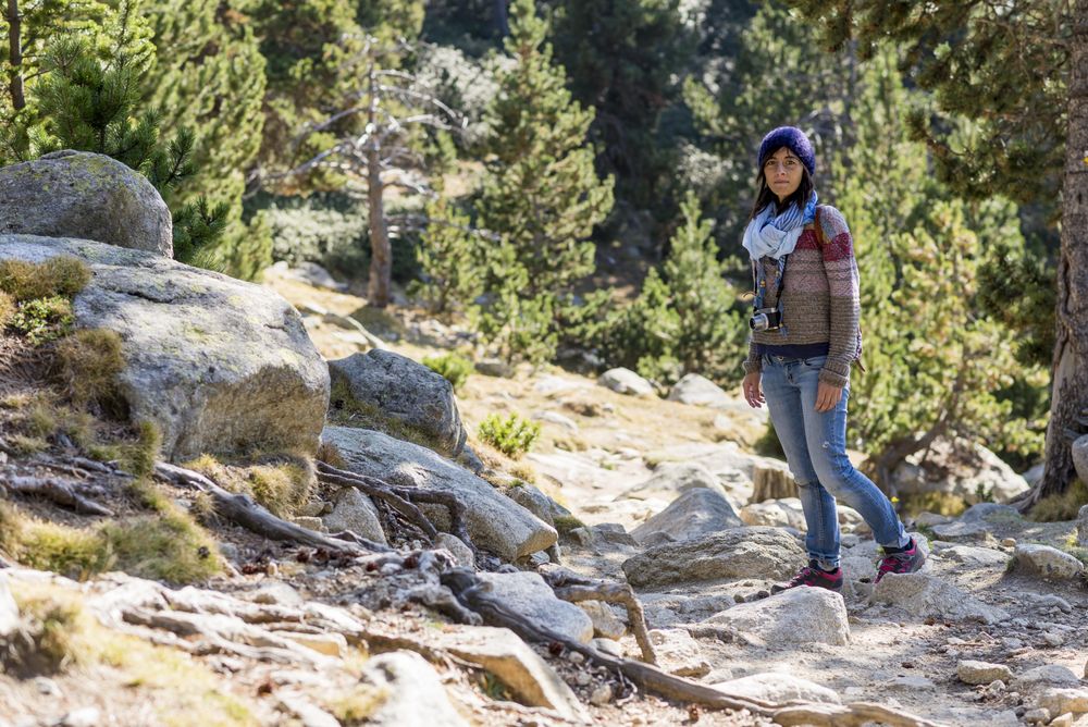 Female standing in rocky forest on sunny day with camera