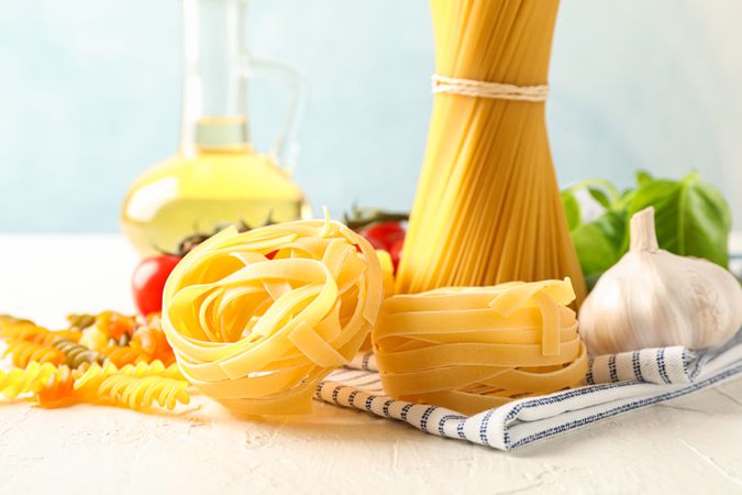 Composition with pasta, tomatoes, garlic, olive oil and kitchen towel on light background, space for text and closeup