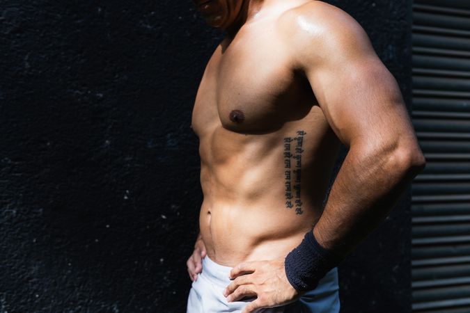 Anonymous positive shirtless Hispanic sportsman near wall