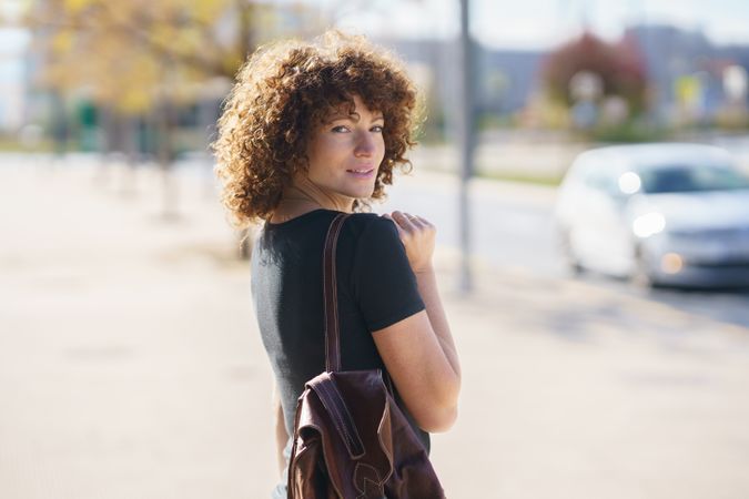 A young woman with beautiful curly hair is happily walking on a sunlit city street