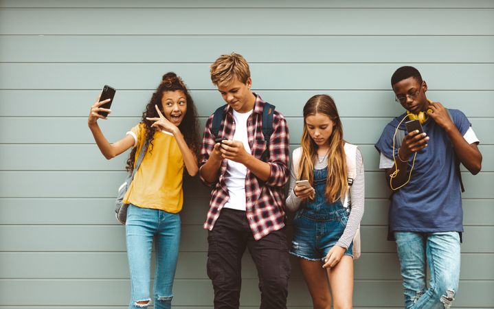 Young girl taking a selfie standing outdoors with her friends looking at their mobile