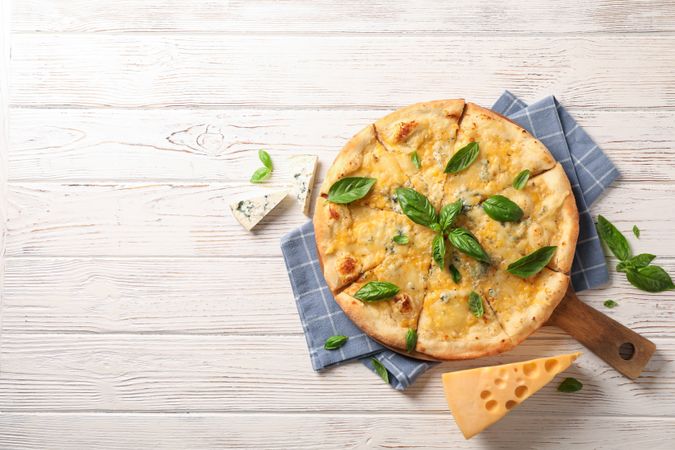 Towel, board, cheese pizza with basil on wooden background, copy space