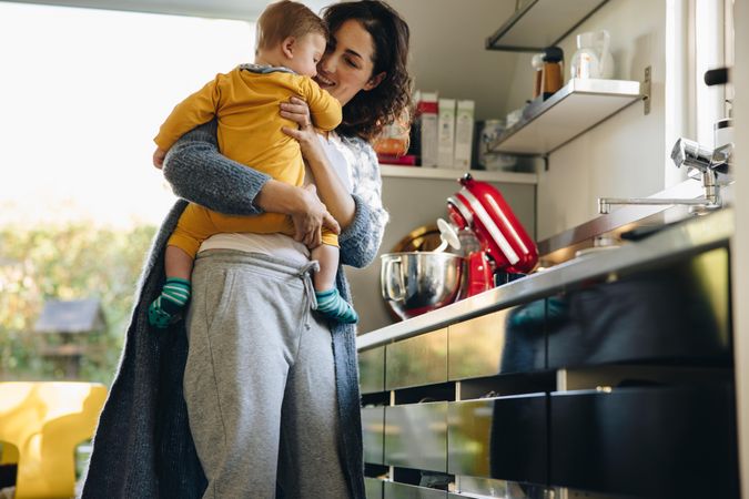Woman carrying son while standing in kitchen