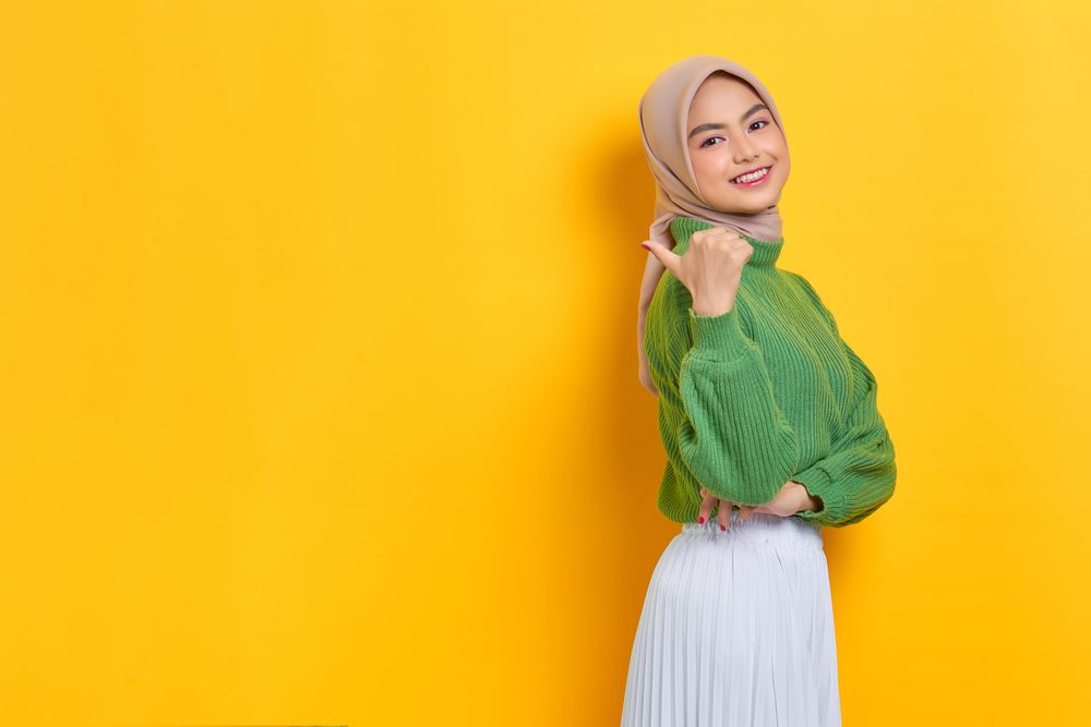 Happy woman in headscarf pointing her thumb behind her