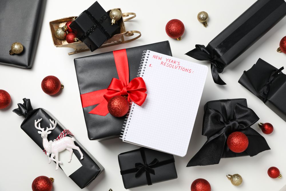 Notepad with list and gift boxes on light background, top view