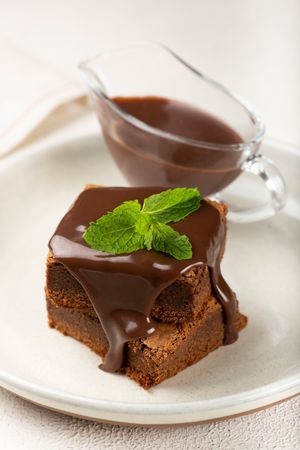 Brownies served with pot of chocolate sauce and mint garnish, vertical
