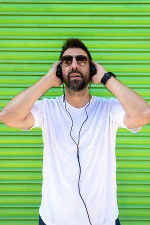 Man wearing sunglasses and holding headphone in front of green background