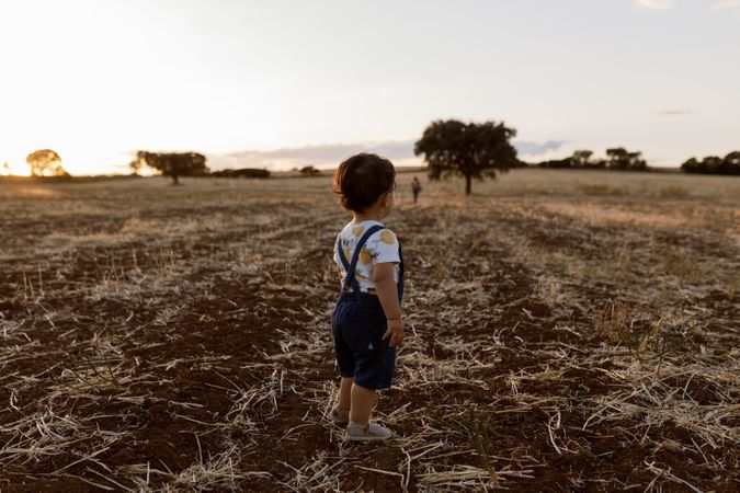 Little boy looking around in a field with trees in the distance