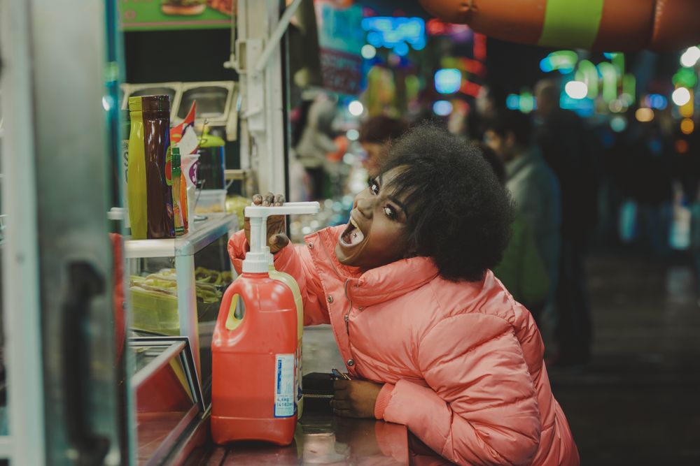 Black woman pretending to eat sauce from diner bottle