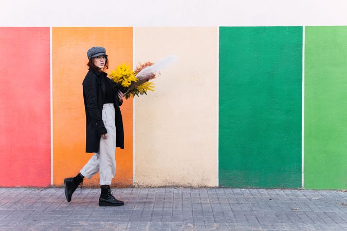 Woman with flowers walking against colorful wall