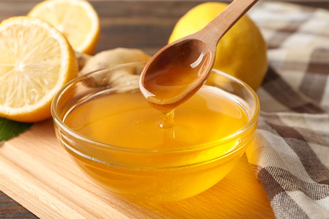 Lemons, bowl with honey and dipper on wooden background, close up